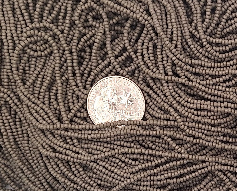 A close-up of many strands of small gray seed beads filling the frame, with a silver coin placed in the center for scale.