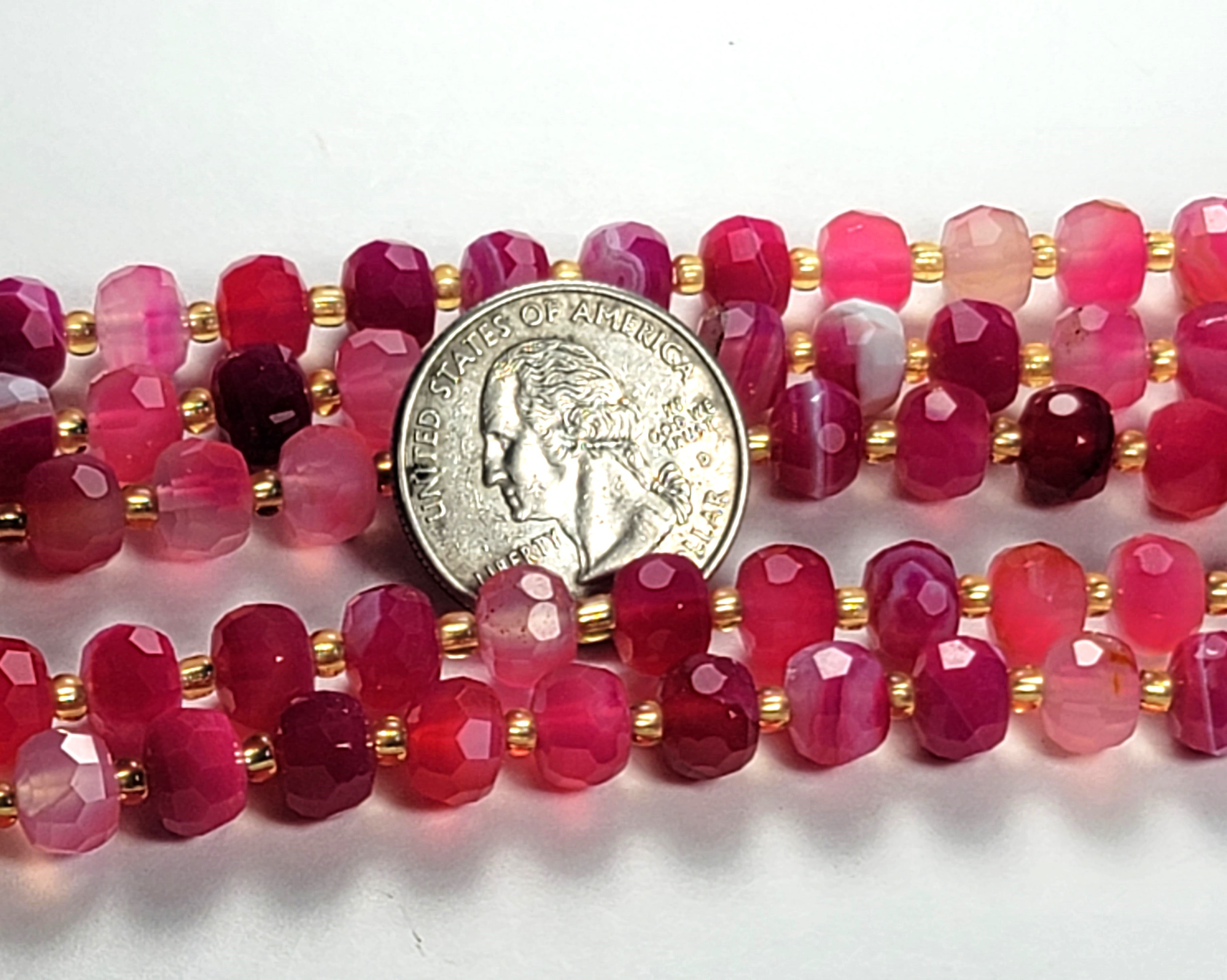 A strand of magenta sardonyx faceted rondelle gemstone beads with a coin for scale.