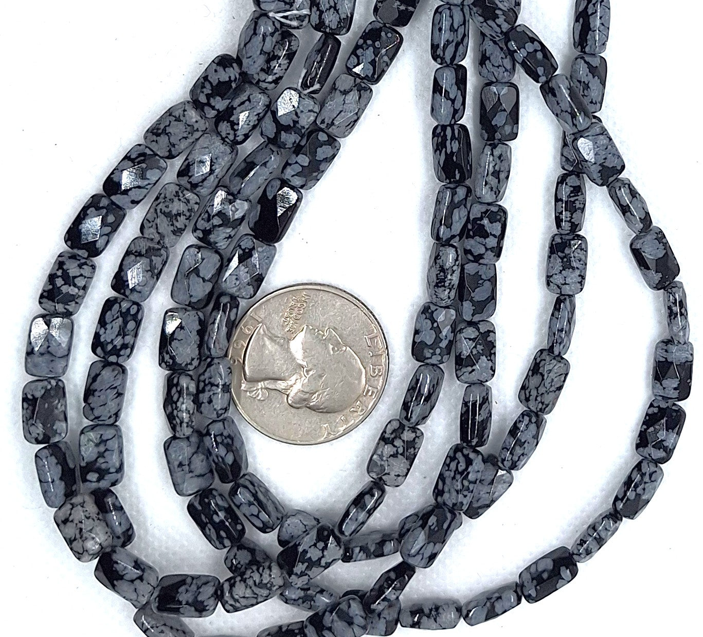 String of gray speckled black beads with a quarter for scale on a white background