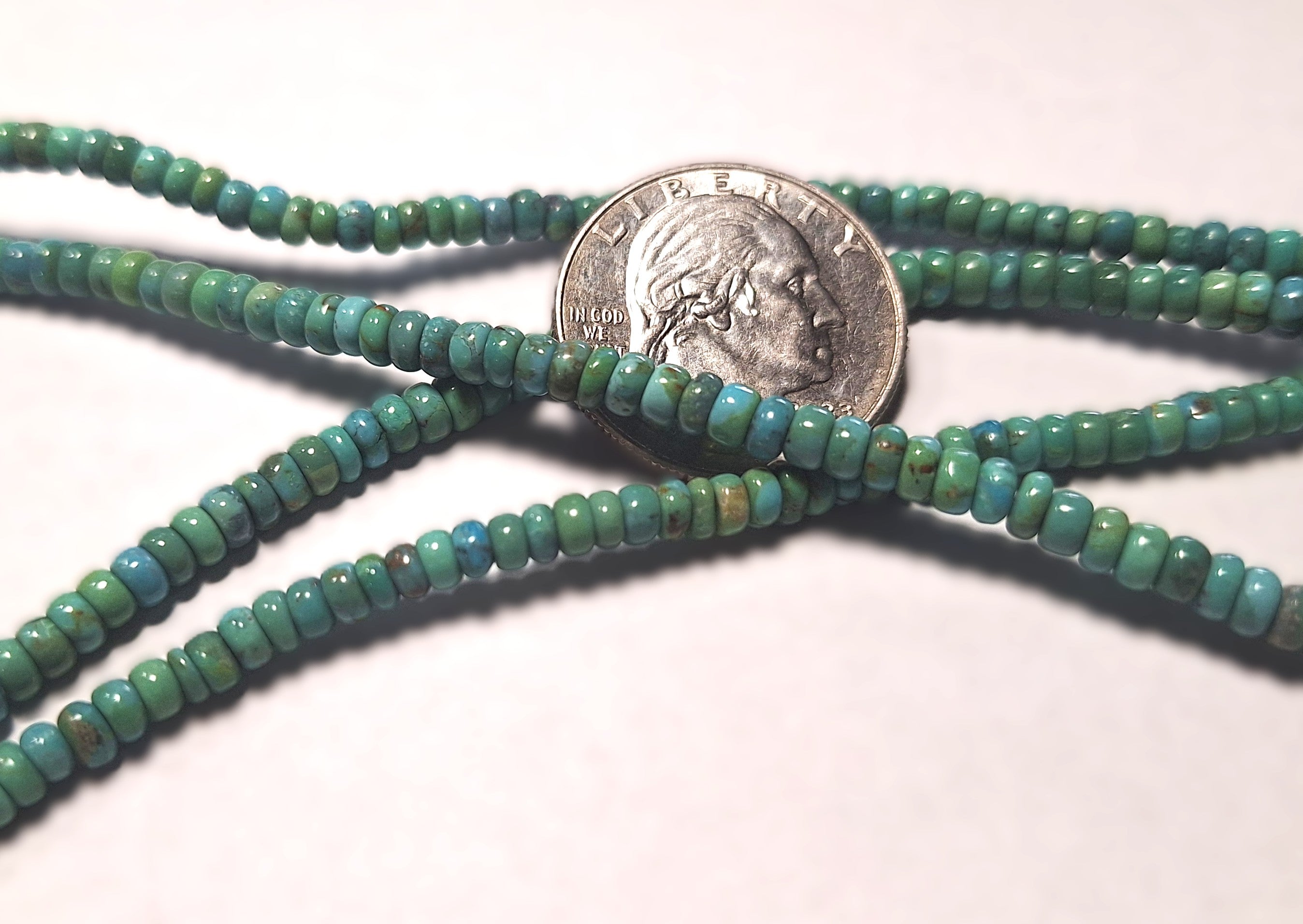 Green beaded strands with a quarter for size comparison on a white background