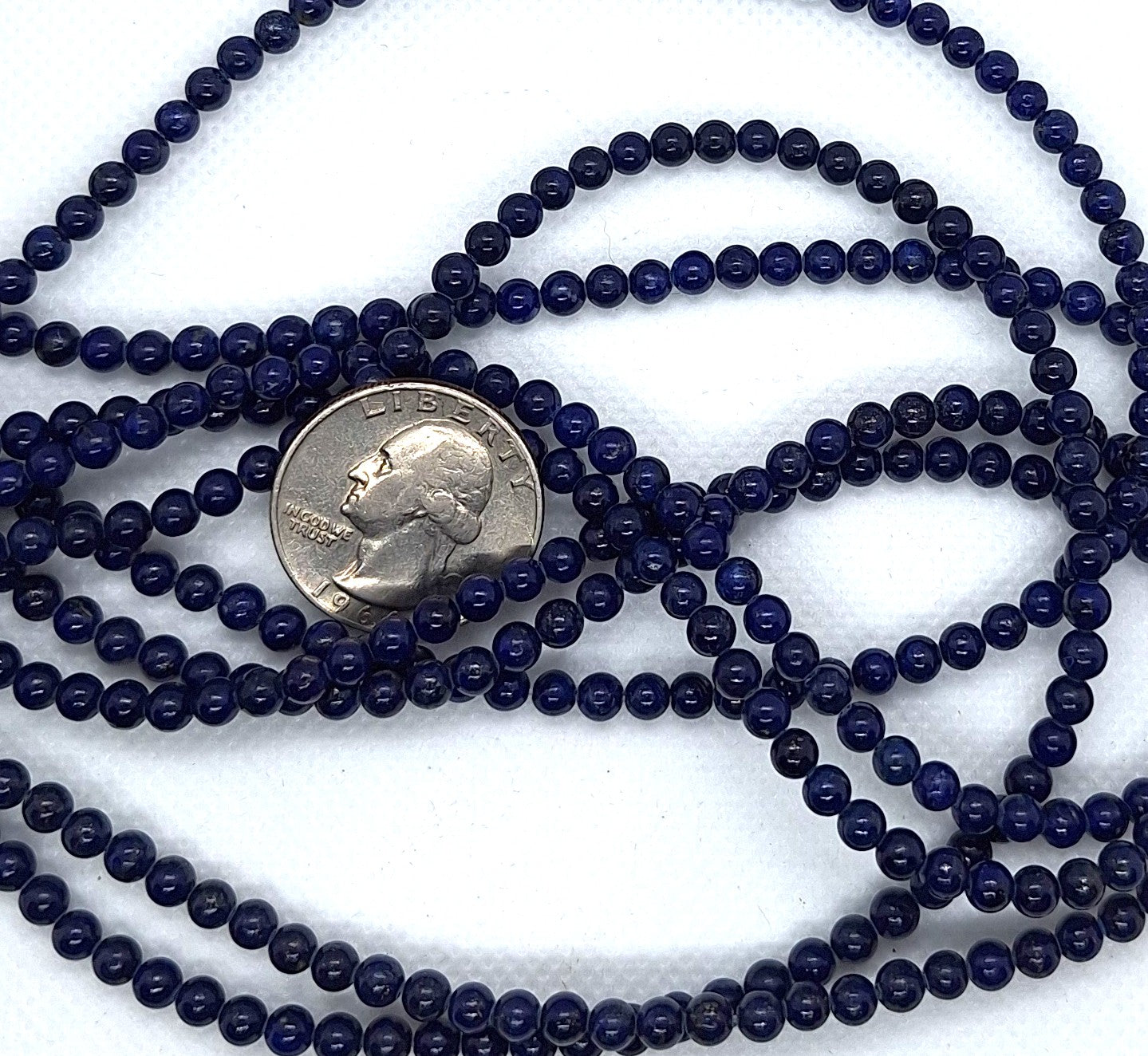 Multiple strands of dark blue beads with a quarter for size comparison on a white background
