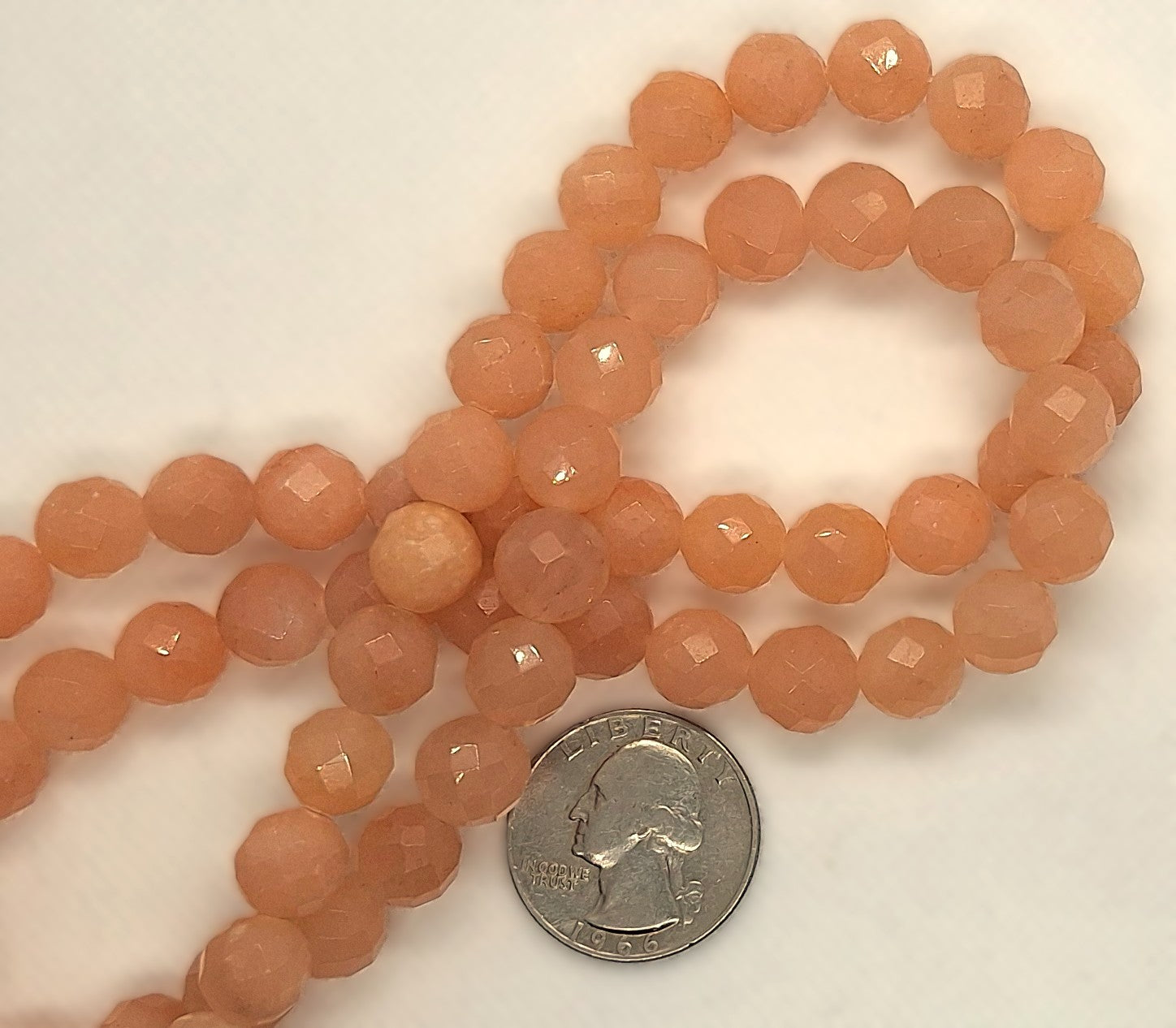 Strand of peach-colored beads with a quarter for size comparison on a white background