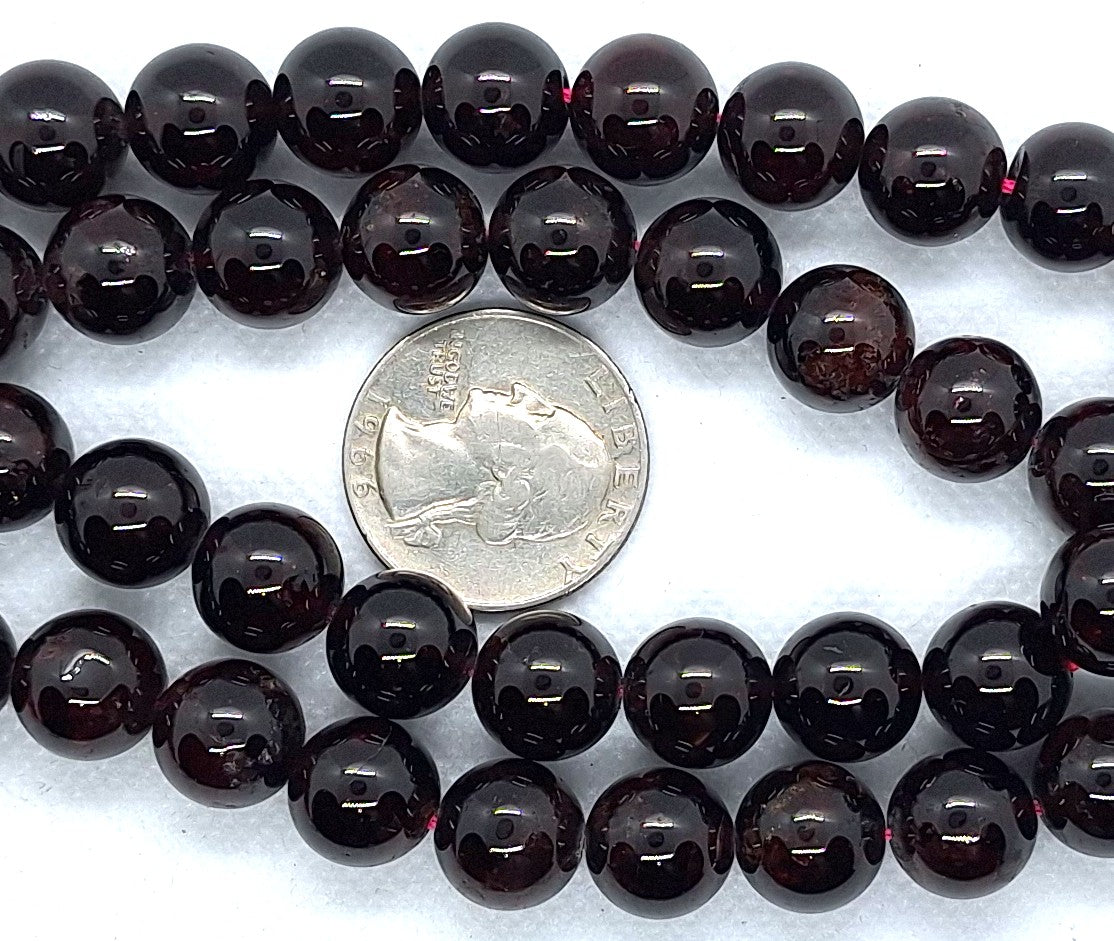 String of dark purple-red round beads with a quarter for size comparison on a white background