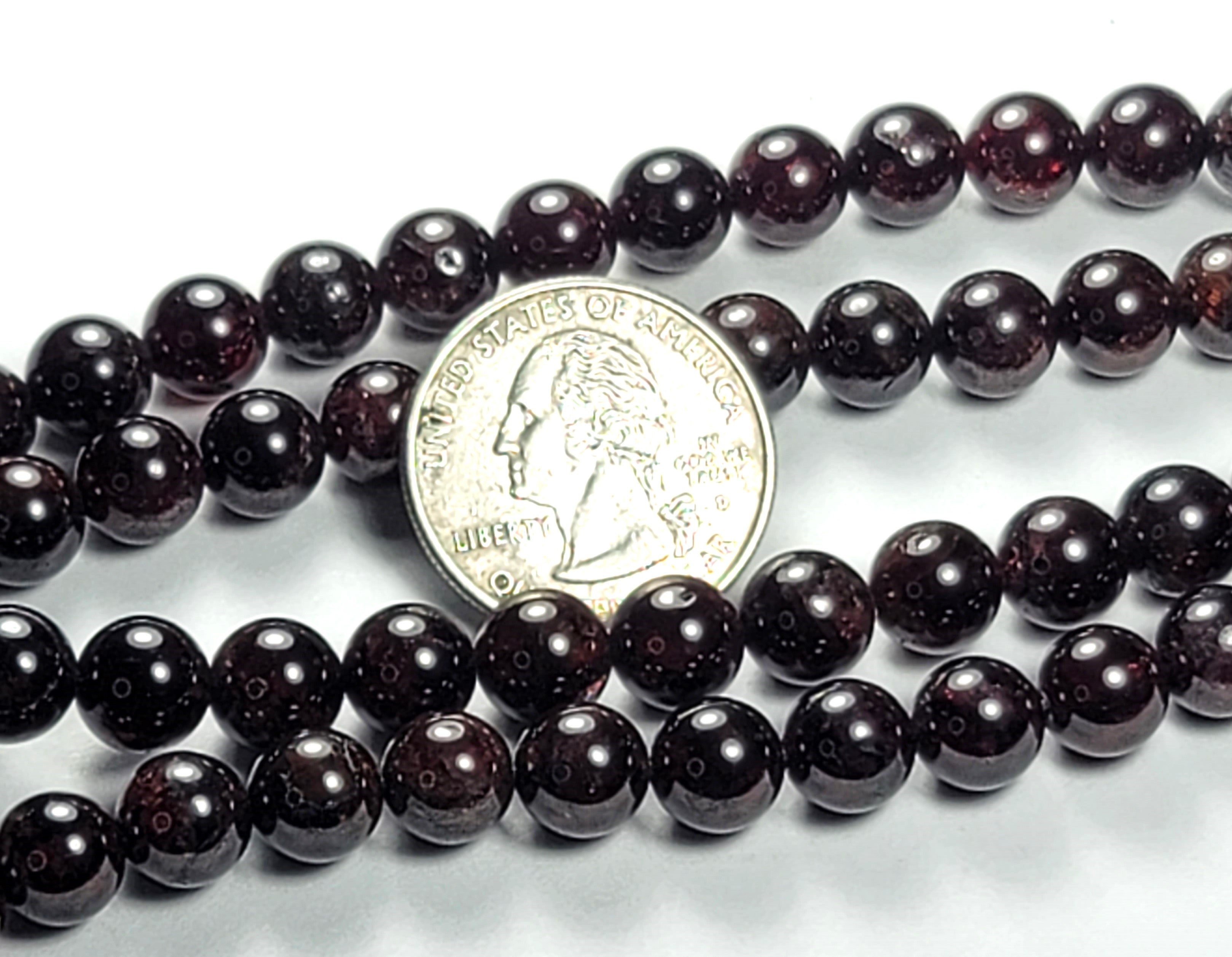A strand of 8mm red garnet round gemstone beads with a coin for size comparison.