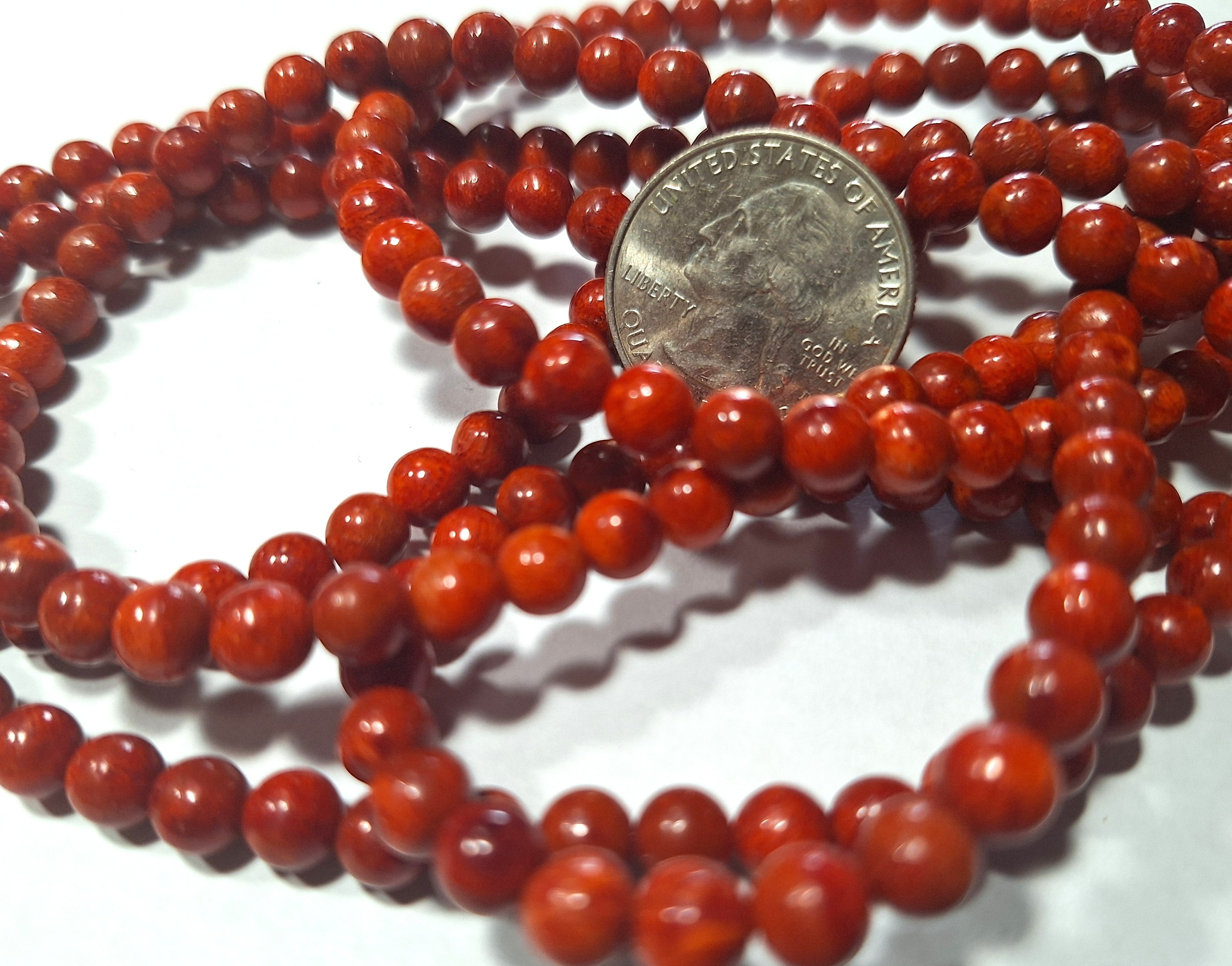 A close-up of a red dyed sponge coral bead next to a coin for scale.