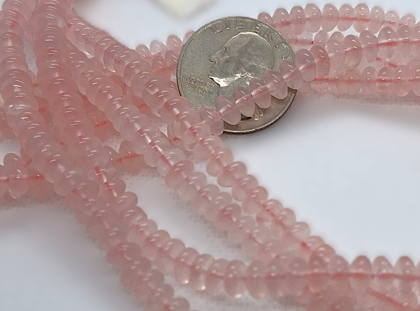 Strand of pink rose quartz beads with a quarter for scale on a white background