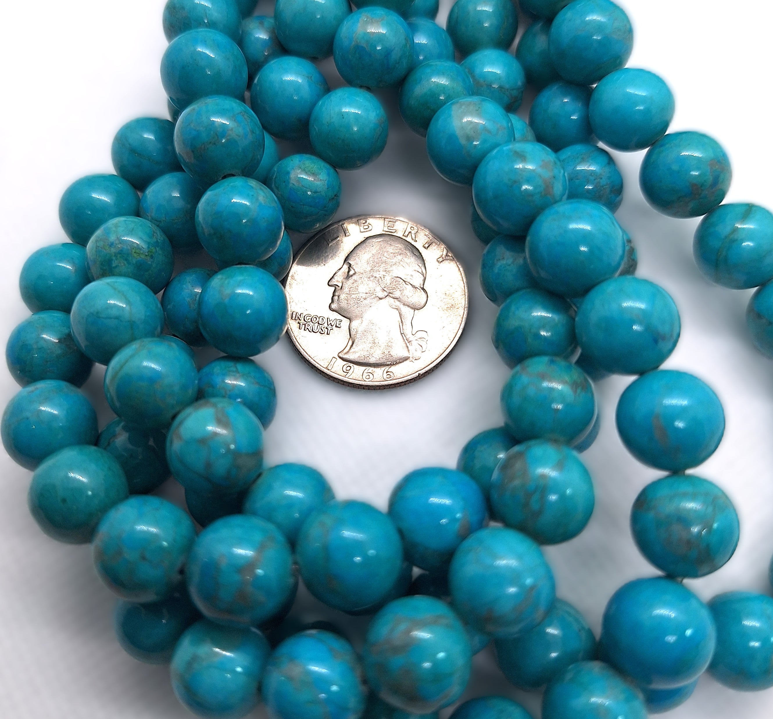 Turquoise-colored howlite beads with a quarter for size comparison on a white background