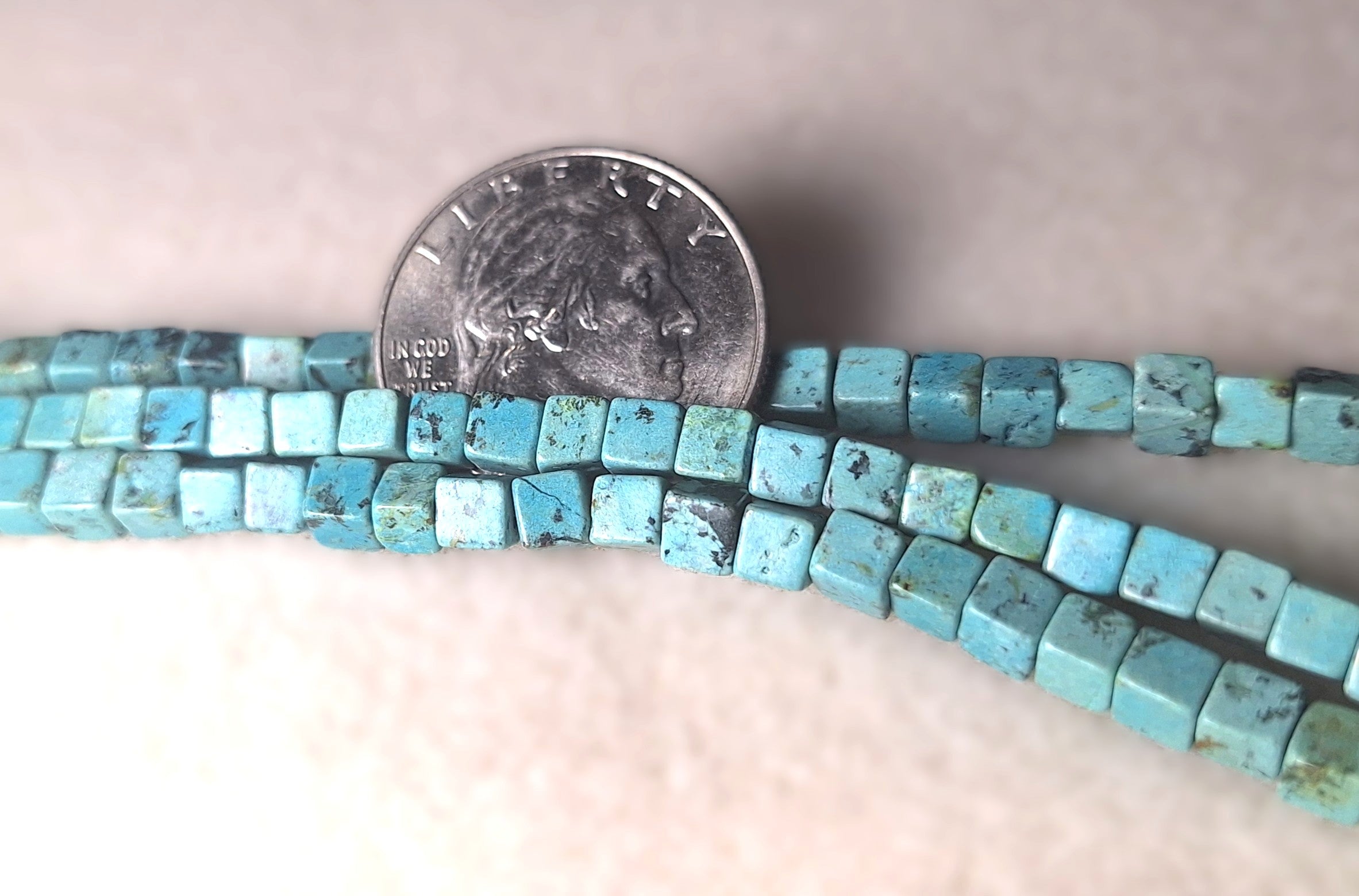African turquoise beads with a quarter for size comparison on a light background