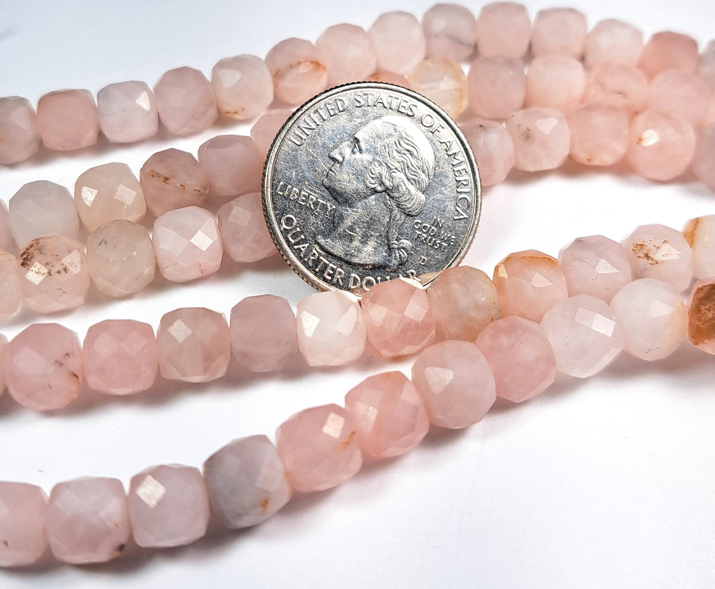 A strand of pink rose quartz faceted cube gemstone beads, with a coin placed for scale.