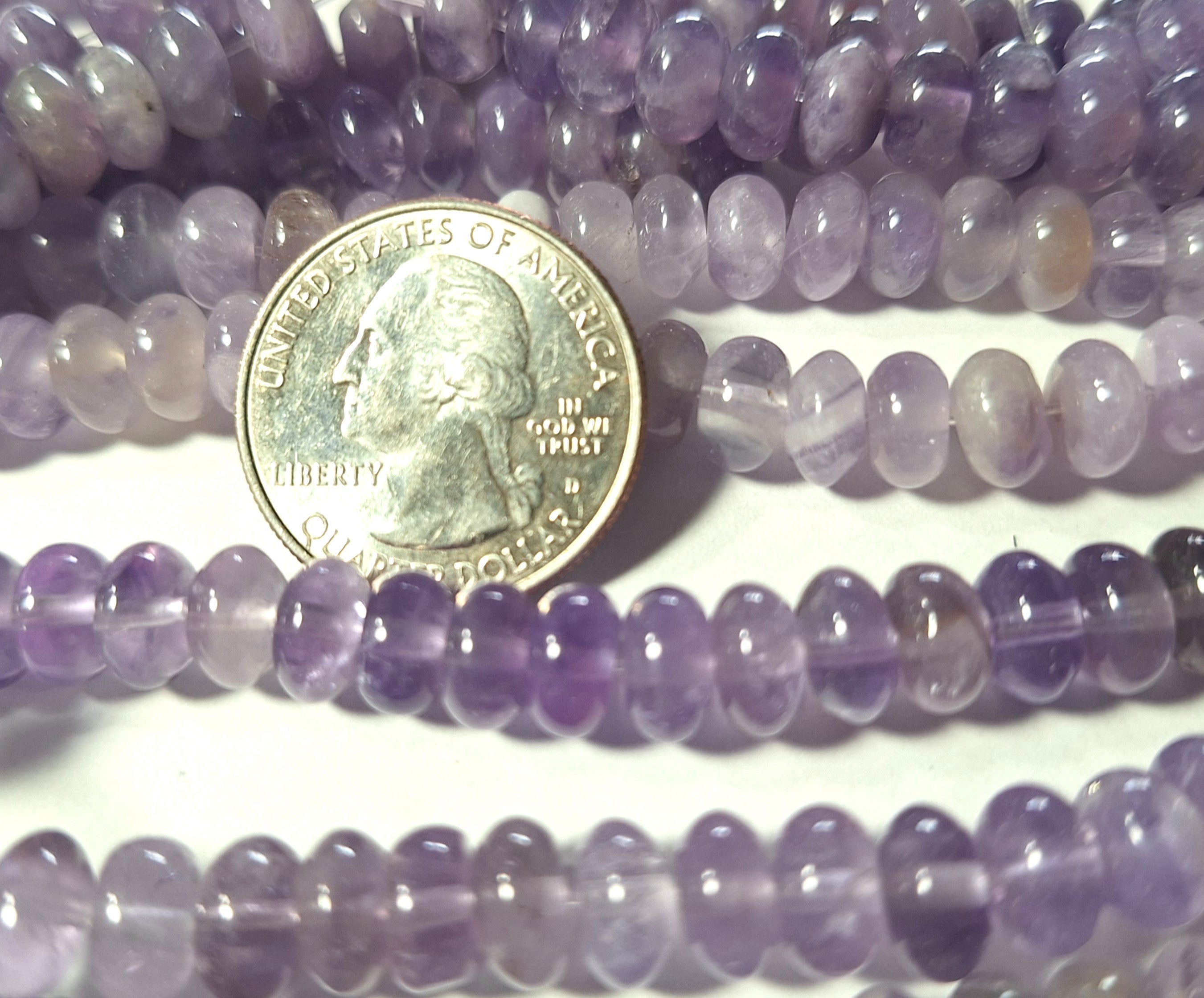 A close-up of smooth rondelle-shaped amethyst gemstone beads alongside a coin for scale.