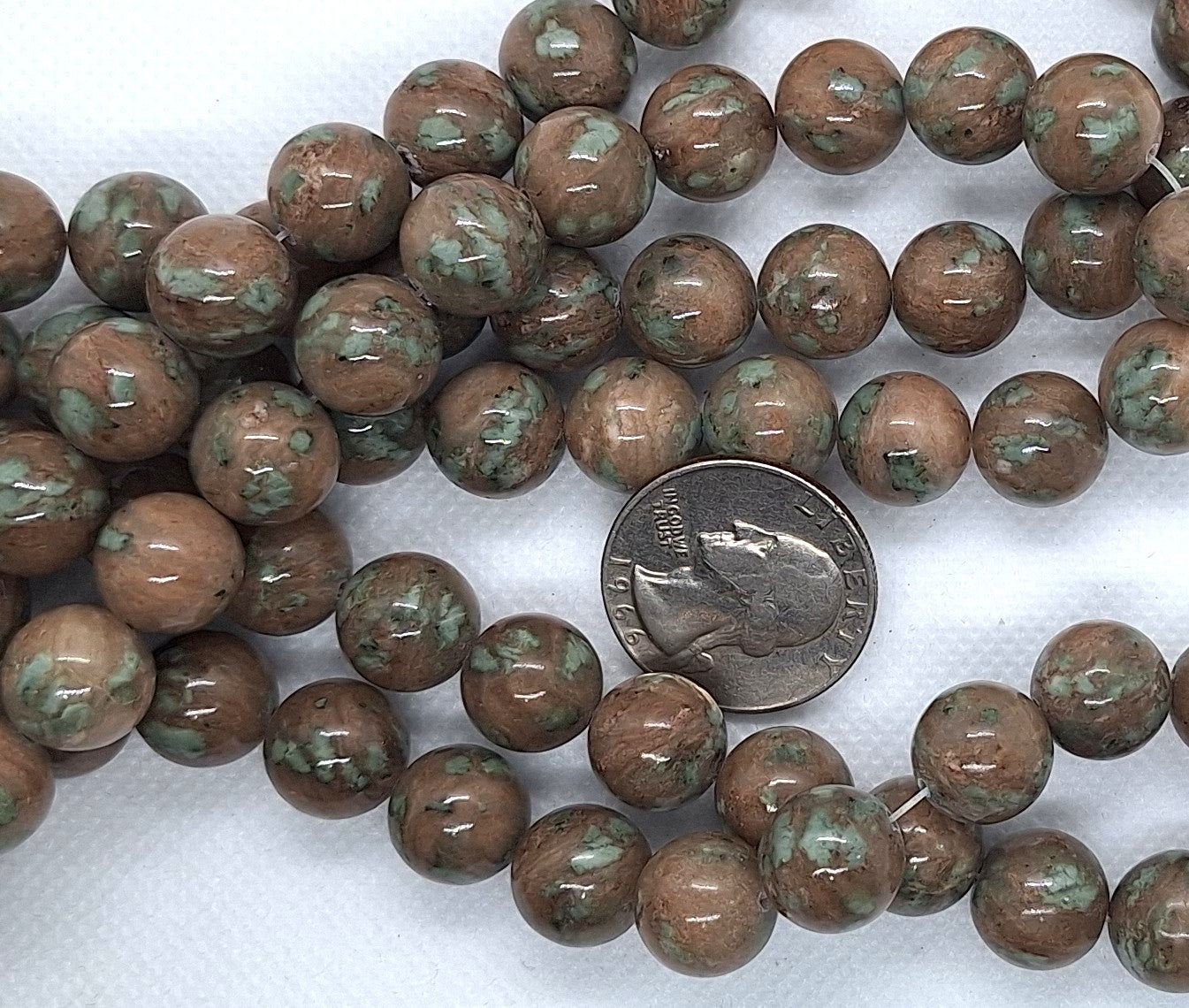 Brown and green speckled beads with a quarter for size comparison on a white background