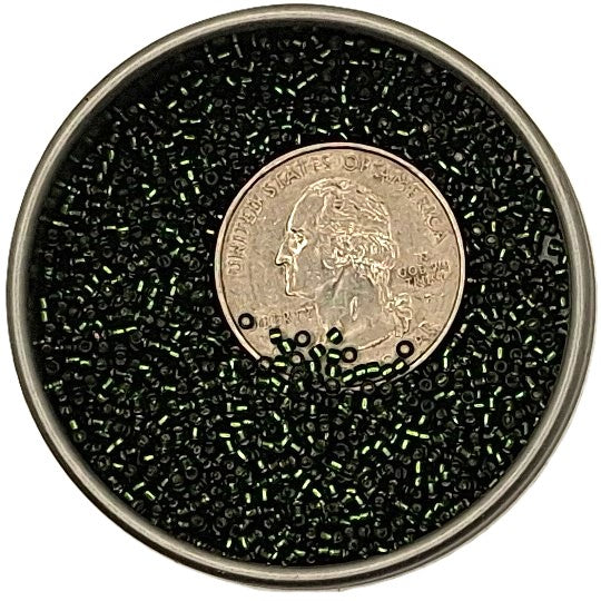 Black seed beads with iridescent green reflections, shown in a round metal container with a US quarter coin in the center for scale, on a white background.