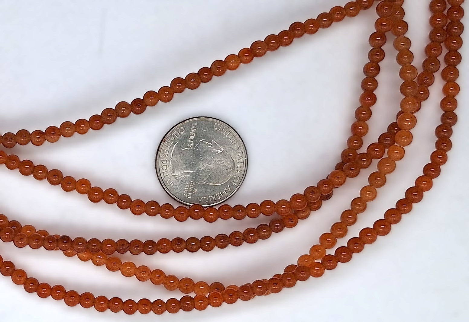 Three strands of orange beads with a quarter coin for size comparison on a white background