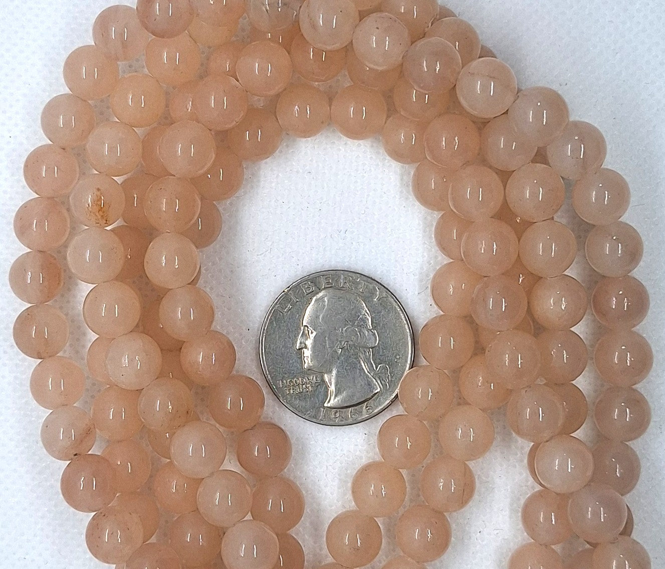 Strand of peach-colored beads with a quarter for size comparison on a white background